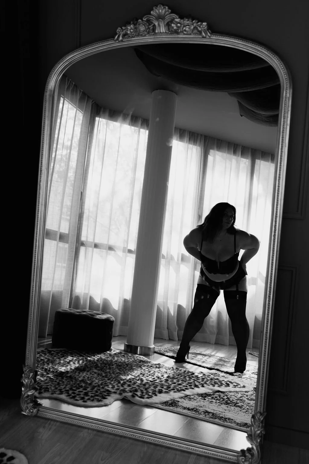 A woman in lingerie and stockings takes a mirror selfie in a room with curtains and a patterned rug.