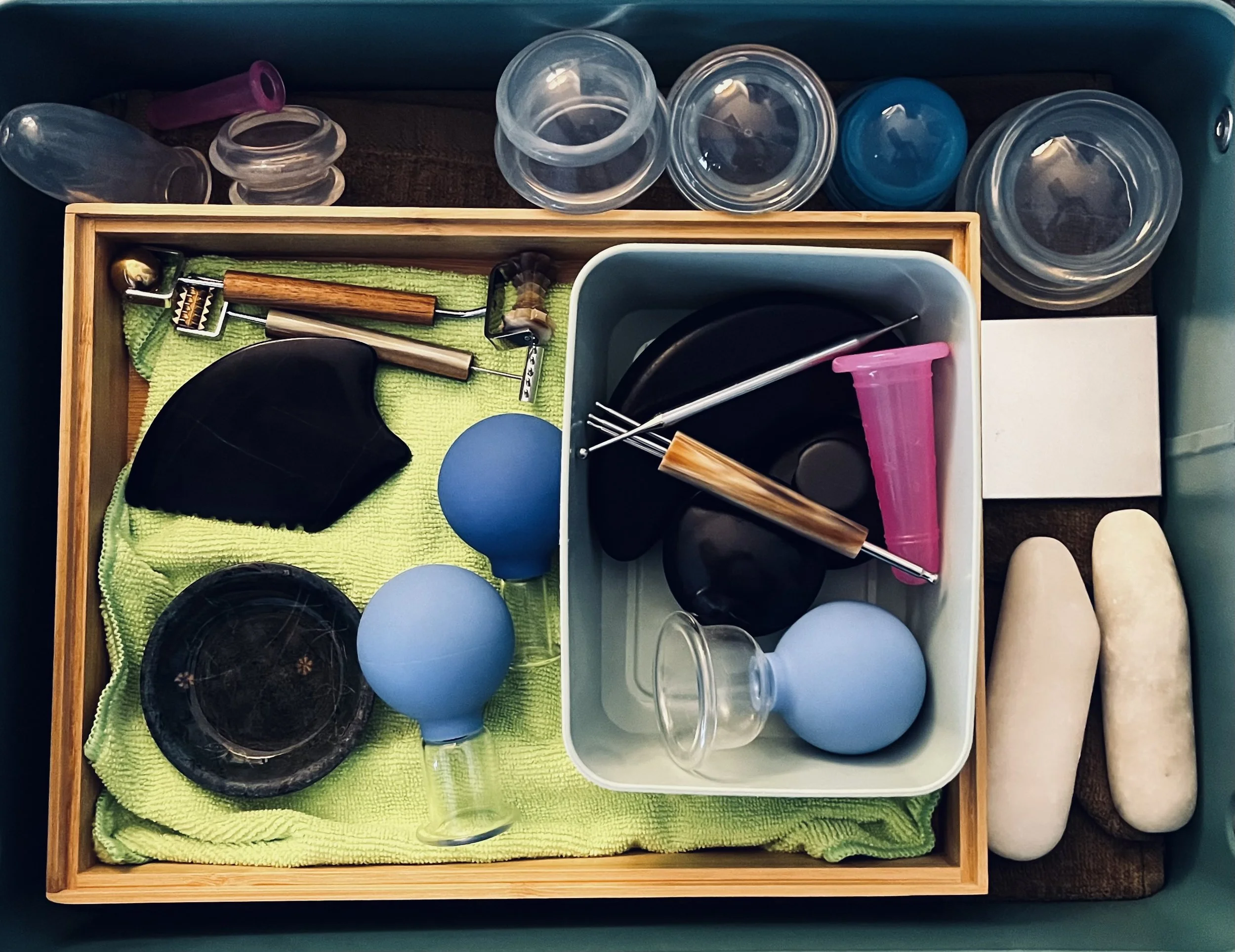 A collection of facial massage tools including glass and silicone massage cup, gua sha stone and stainless steel rollers.