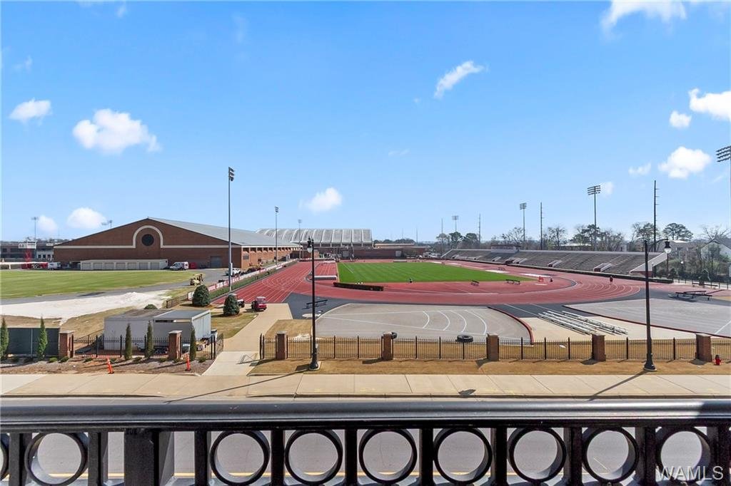Empty outdoor running track and sports field at a high school or stadium with a brick building and bleachers in the background.