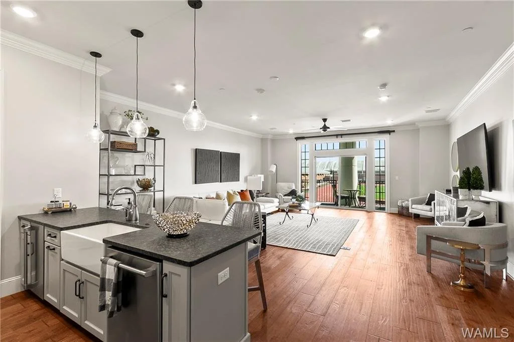 Open-concept living room and kitchen area with hardwood floors, white walls, a gray kitchen island, and seating near sliding glass doors leading to a balcony.