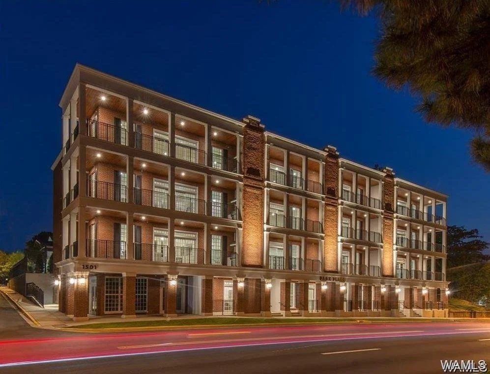 A multi-story residential building at night with exterior lights, brick facade, balconies, and large windows, located at 1507 Park Place.