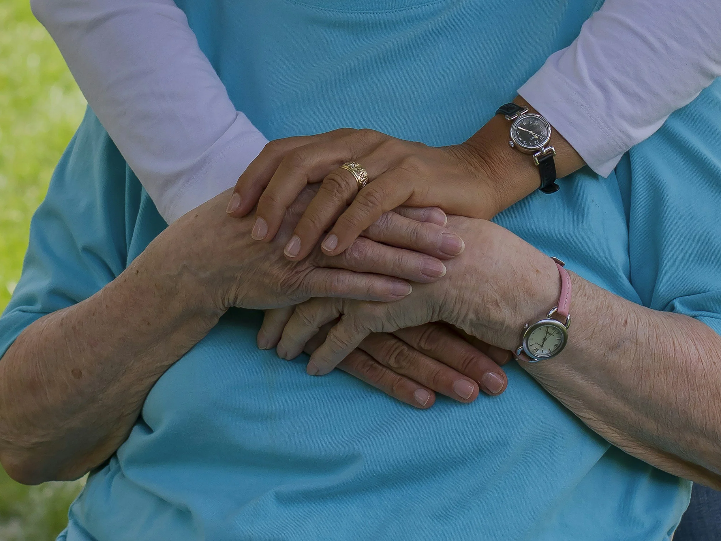 Close-up of three hands, older and younger, placed on top of each other, with the background of green grass, symbolizing care and support.
