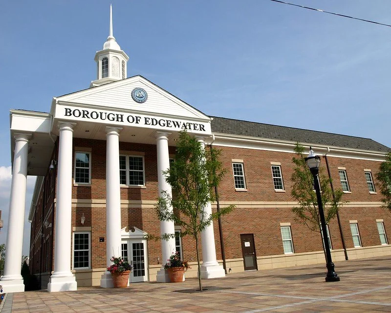 Town hall building with white columns and a sign that reads 'Borough of Edgewater', with trees and street lamps in front.