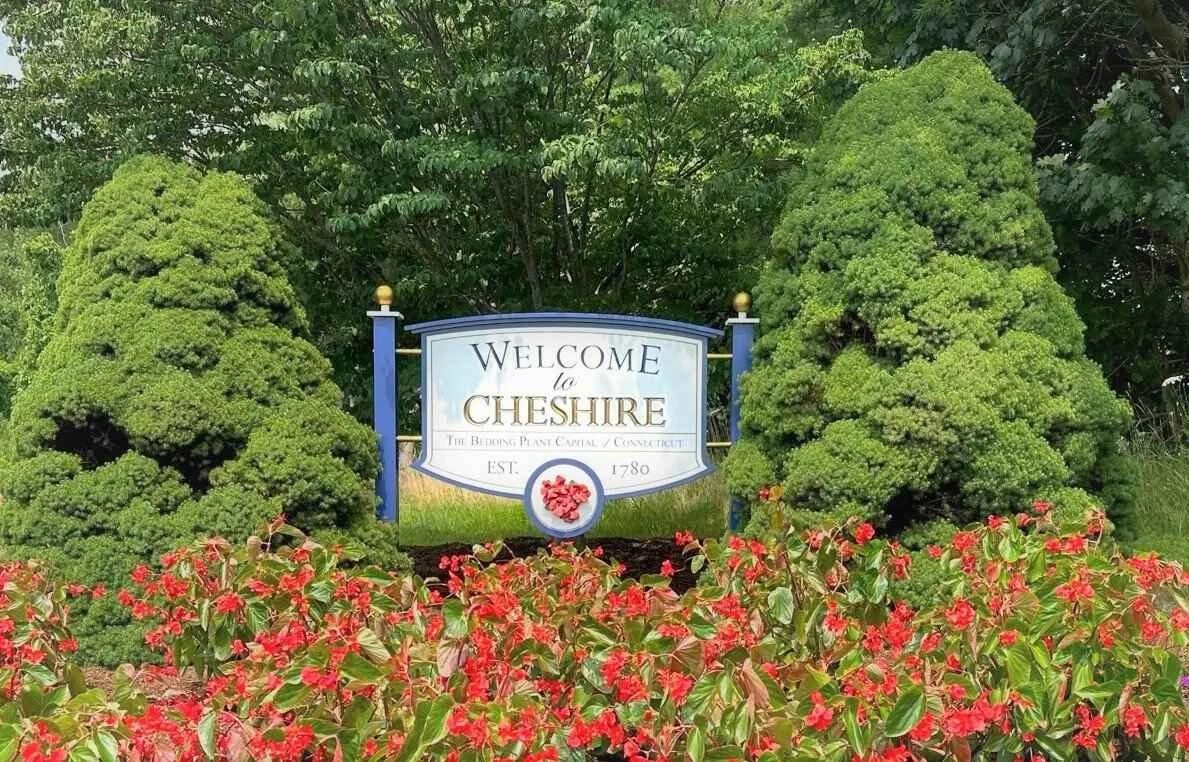 Welcome sign in Chesire surrounded by trimmed bushes and colorful flowers.