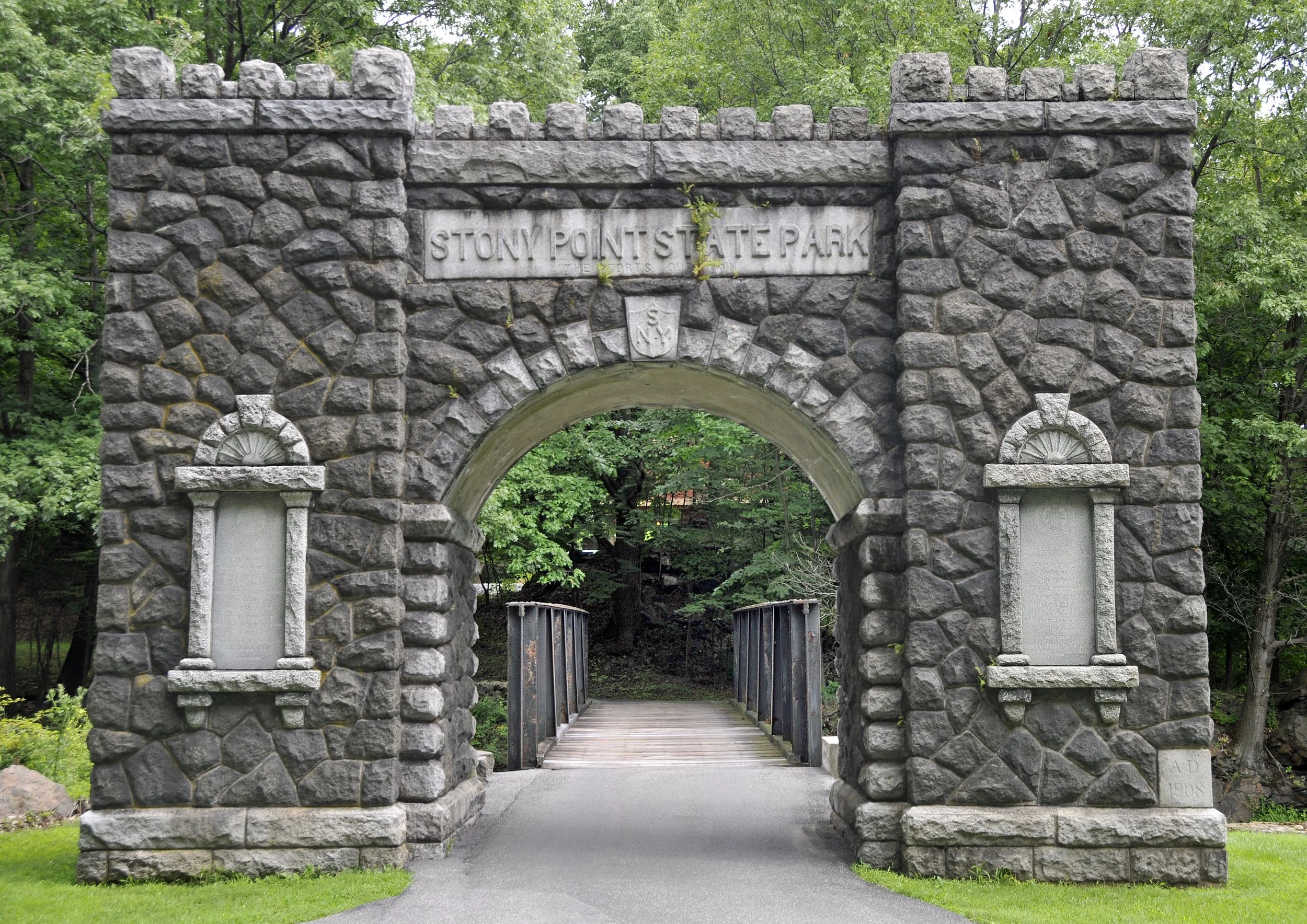 Stone archway entrance to Stony Point State Park with pathway and green trees in the background.