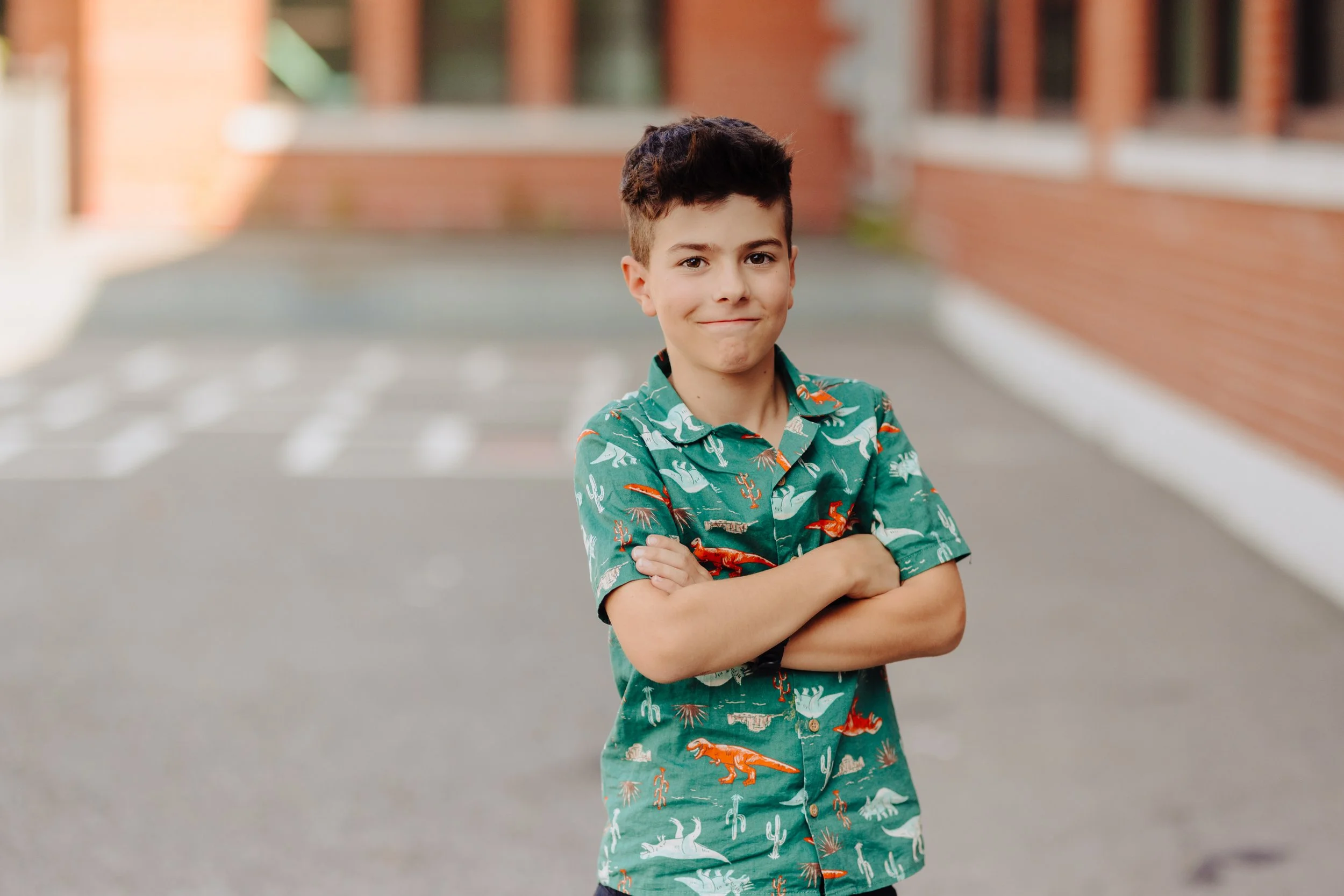 Un garçon souriant aux bras croisés porte une chemise verte à motifs colorés, dans un style de photographie scolaire réalisée par des photographes au Québec.