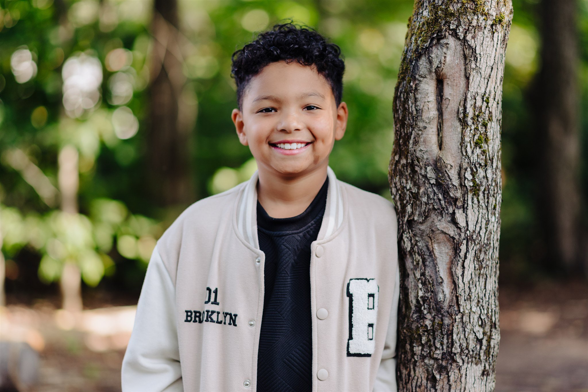 Un garçon souriant se tient près d’un arbre dans un parc, dans un style de photographie scolaire réalisée par des photographes au Québec.