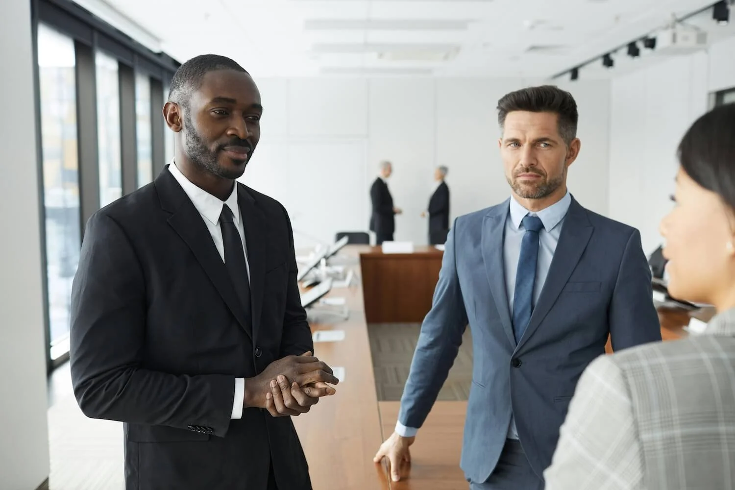 Two men wearing suits listen to another person talking in an office environment