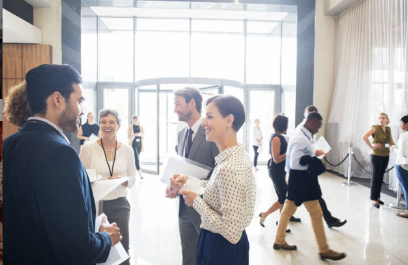 People engaging in conversations at a professional networking event in a spacious, well-lit venue with large glass doors.