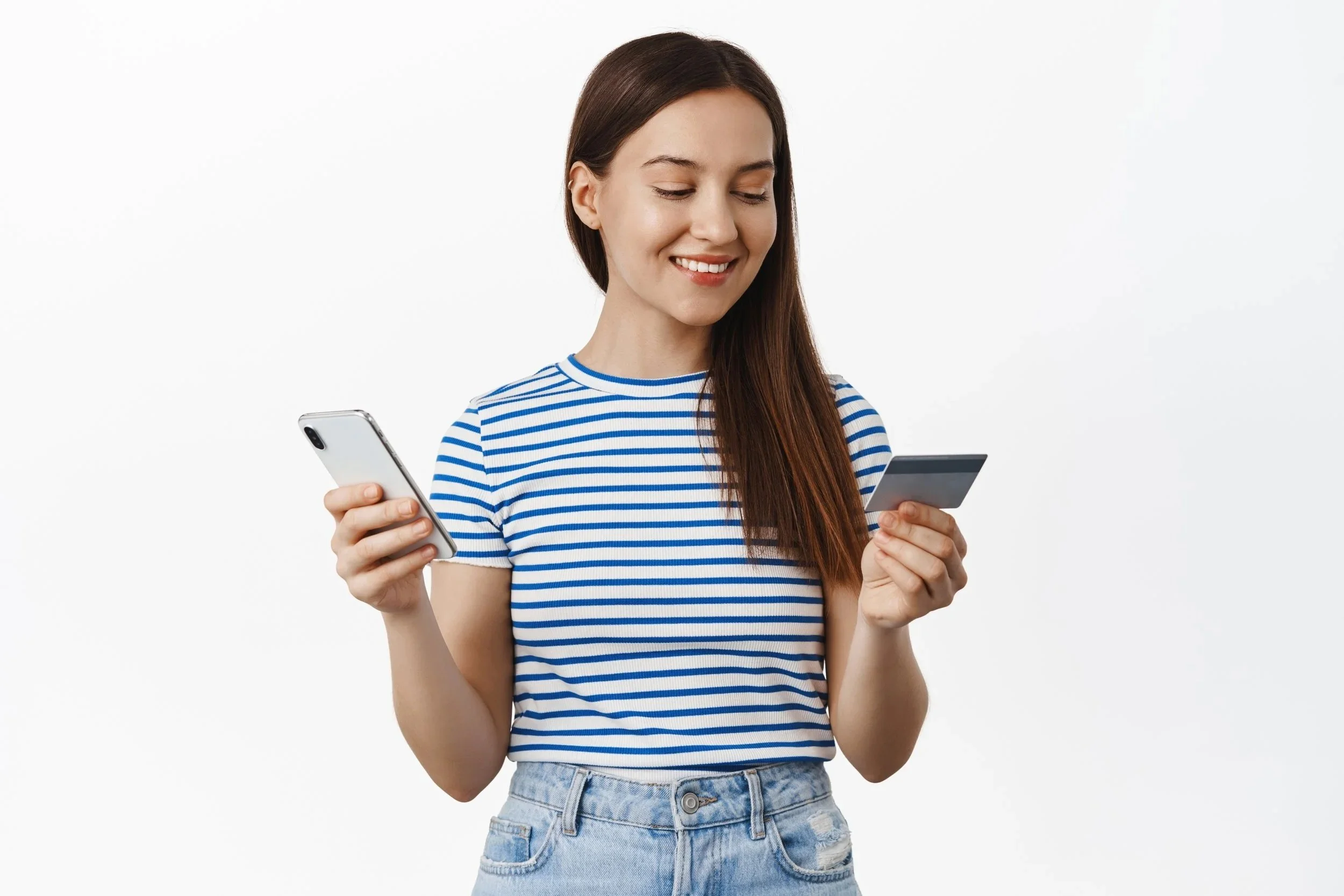 A young woman holding a smartphone in one hand and a credit card in the other, smiling while looking at her credit card. Credits for FreePik
