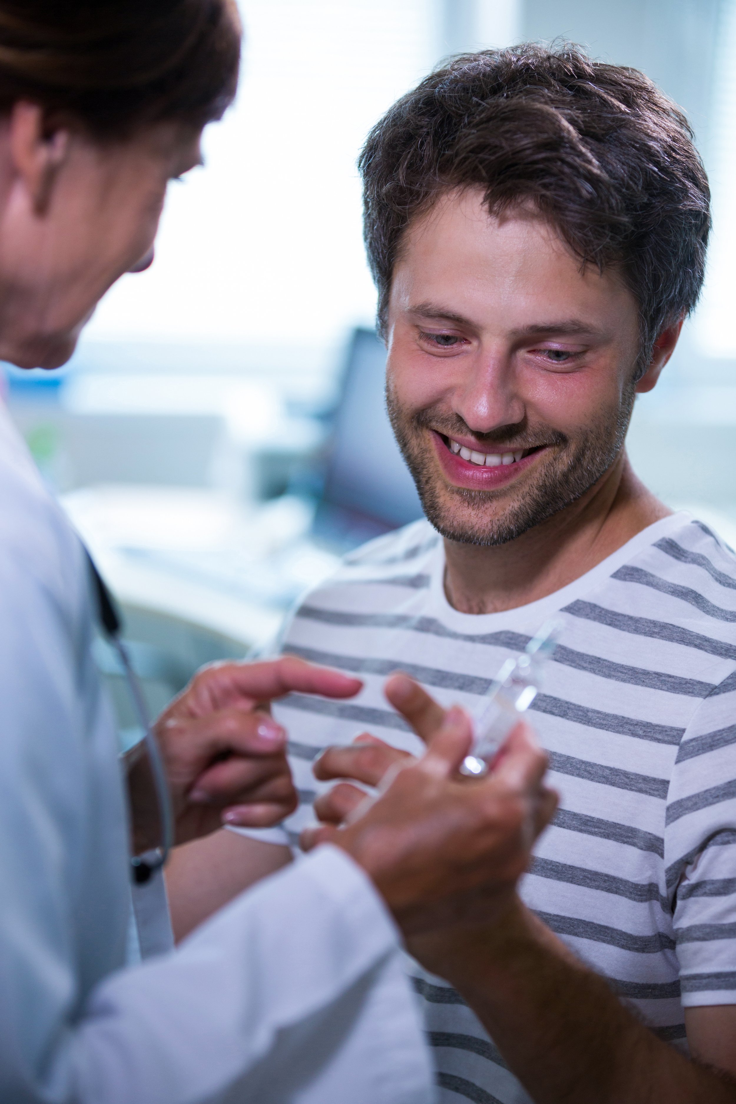 A young man in a striped shirt smiling as he receives a vaccination shot from a healthcare professional in a clinical setting. Credits for FreePik