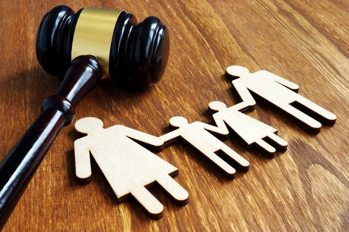 A wooden gavel and wooden figures of a family with two adults, a child, and a baby on a wood surface.