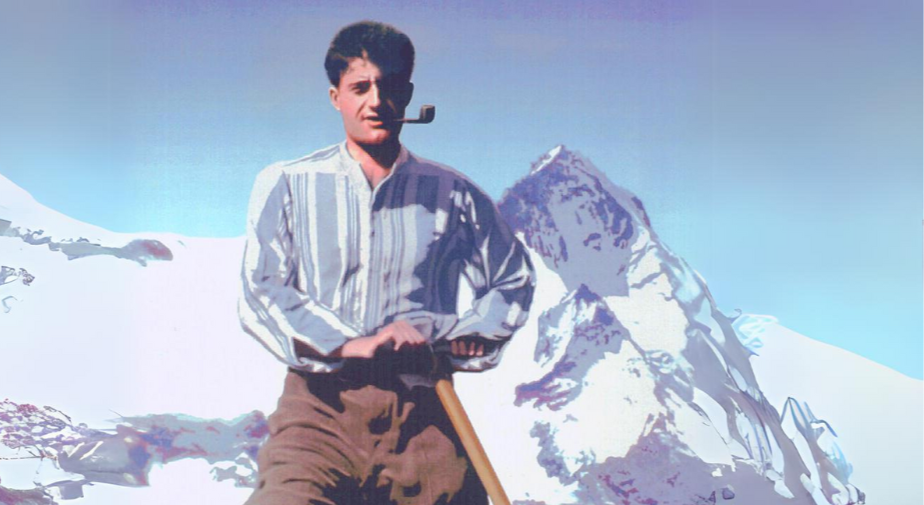 A man standing on snow with a mountain in the background, smoking a pipe, holding an ice axe.