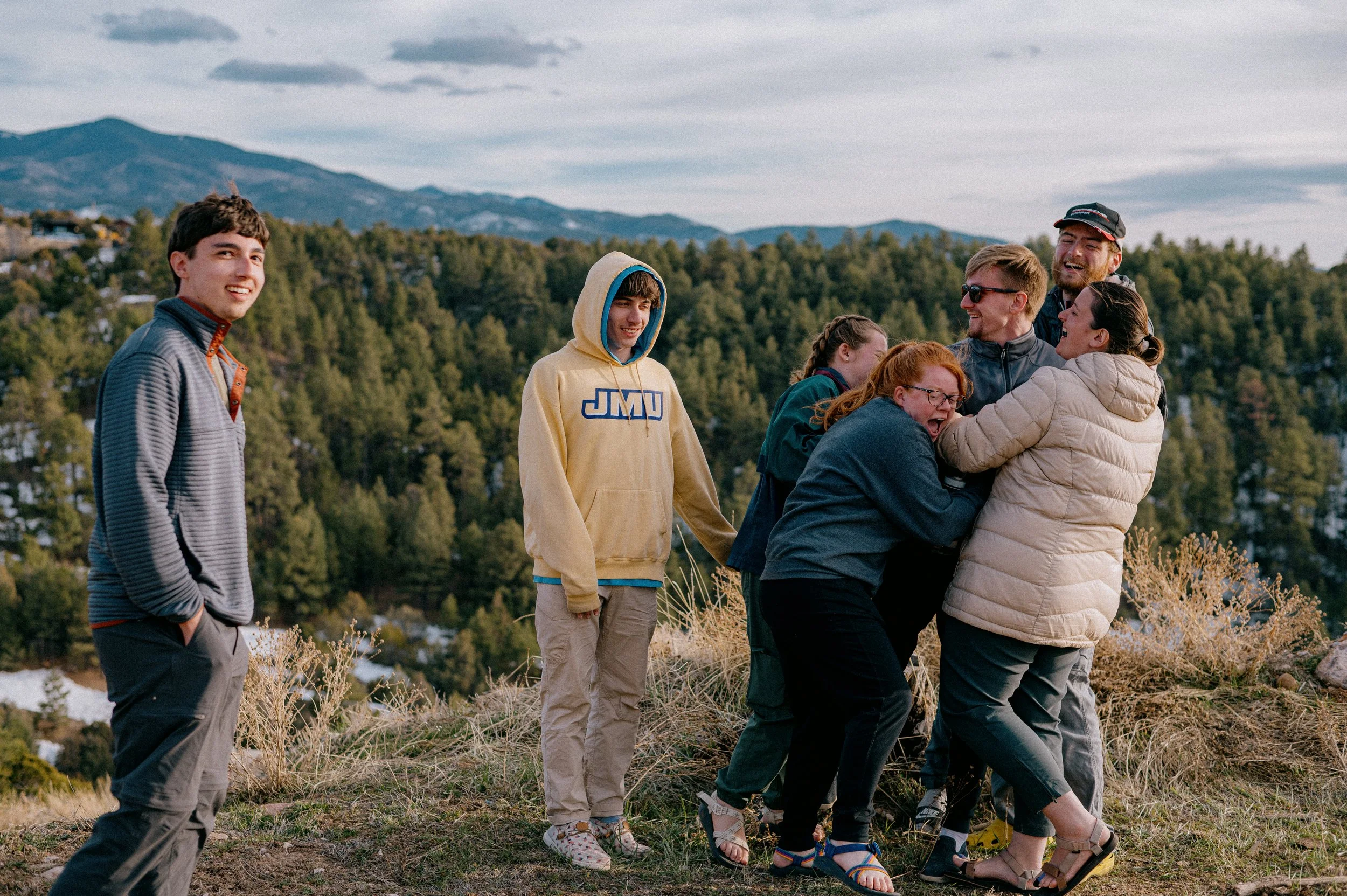 Group of people outdoors, enjoying a playful moment and laughter, with a background of mountains and trees.