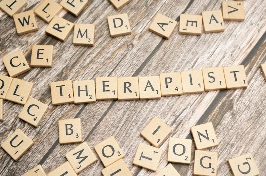 Scrabble tiles spelling out the word "THERAPIST" on a wooden surface.
