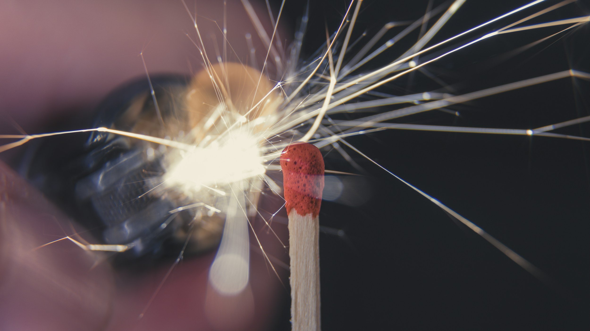 Close-up of a match being struck, sending sparks flying against a dark background