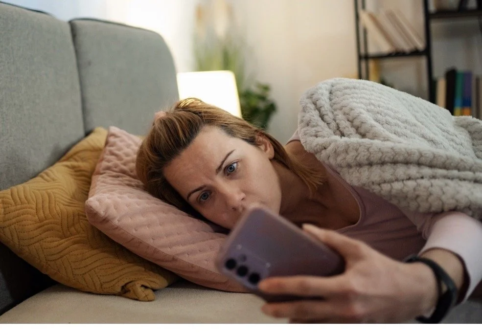 Woman lying on couch doomscrolling phone at night — therapist burnout and anxiety