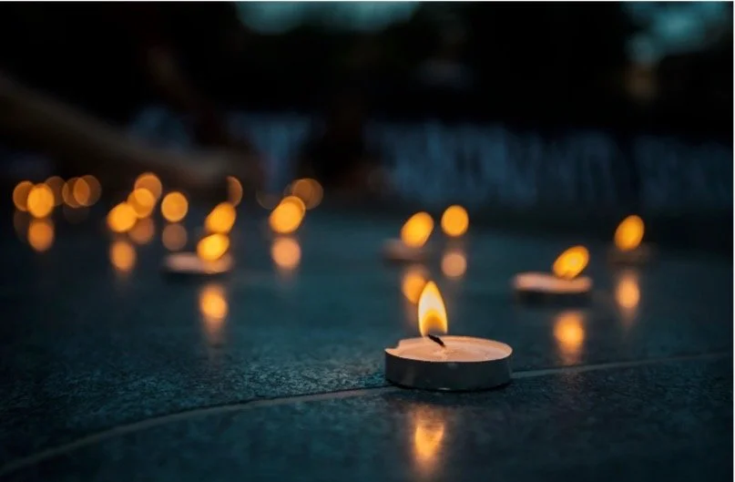 Small tealight candles glowing on dark water at dusk, their light reflected and softly blurred