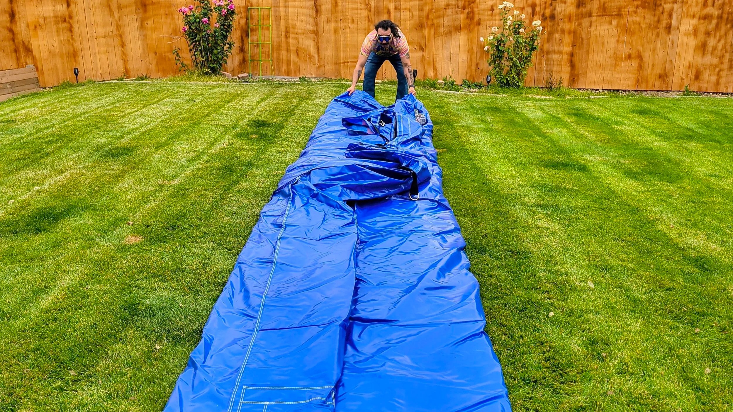 Person laying out a blue tarp on a backyard lawn to prep for an inflatable setup.