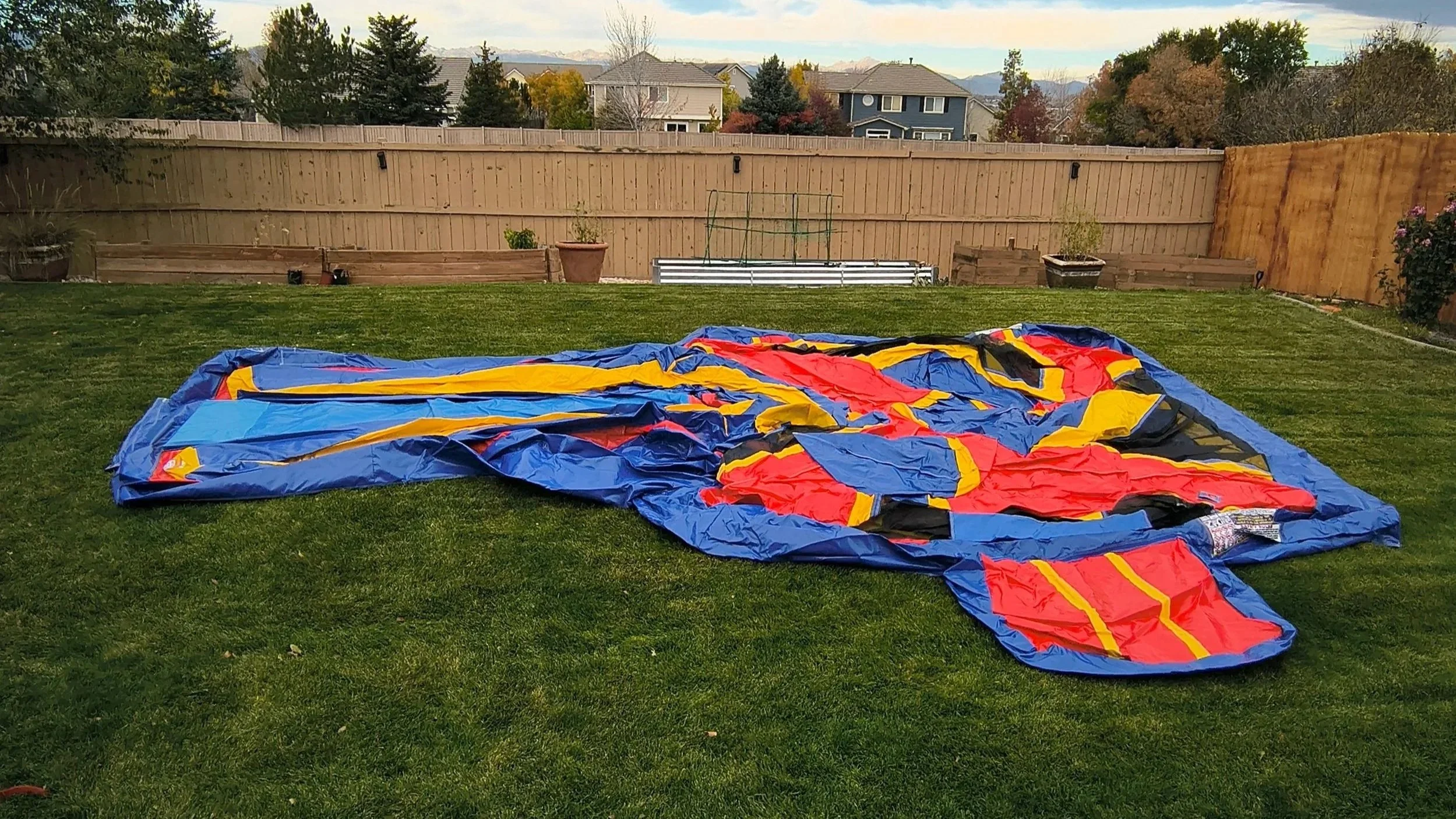 Backyard setup prep with a long blue ground cover laid out on grass while a person positions it for an inflatable rental.