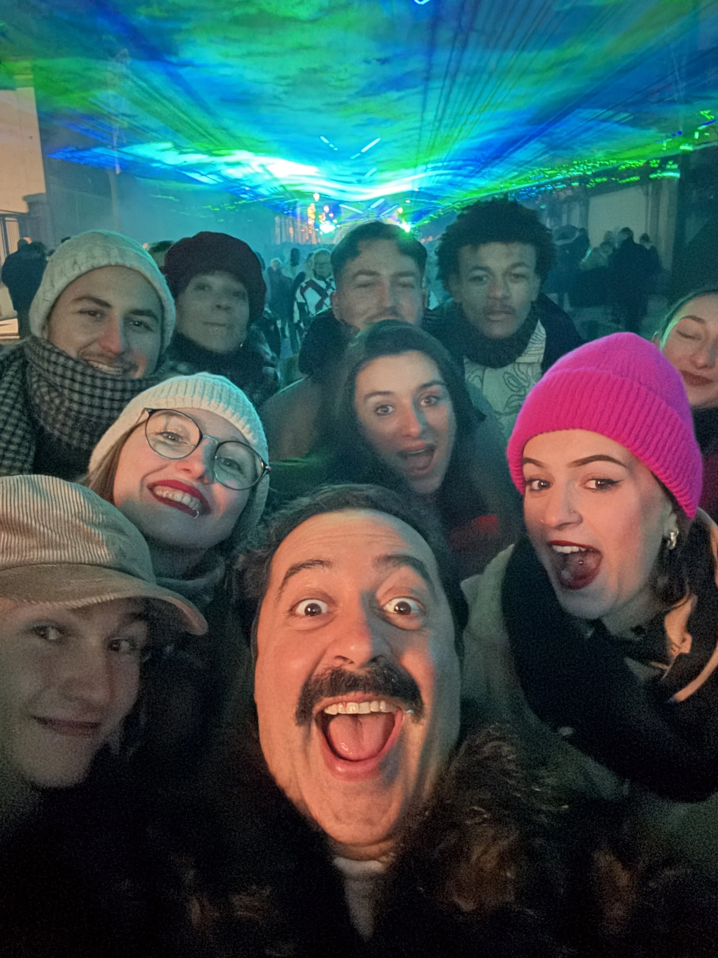 Group of people taking a selfie at a lively event with colorful lights and a crowded background.