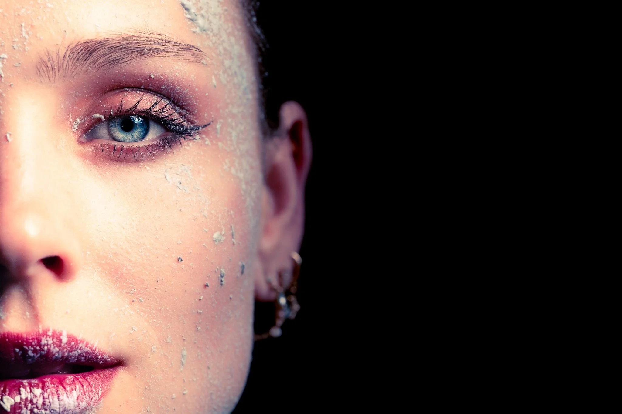 Nahaufnahme eines Gesichtes mit blauen Augen, geschminkten Lippen und pudrigem Make-up.