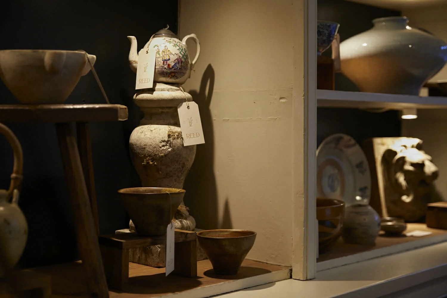 Display of antique ceramic bowls, vases, and decorative objects on wooden shelves in a boutique store.