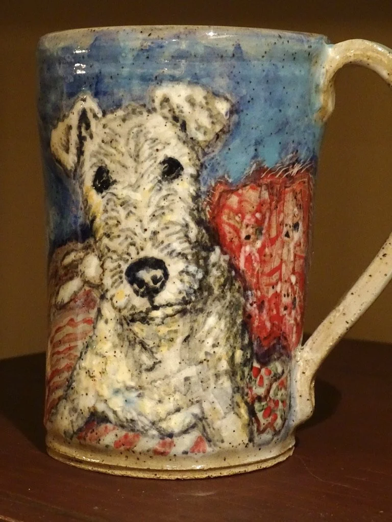 A ceramic mug featuring a painted dog, possibly a West Highland Terrier, with a background of red and blue colors.