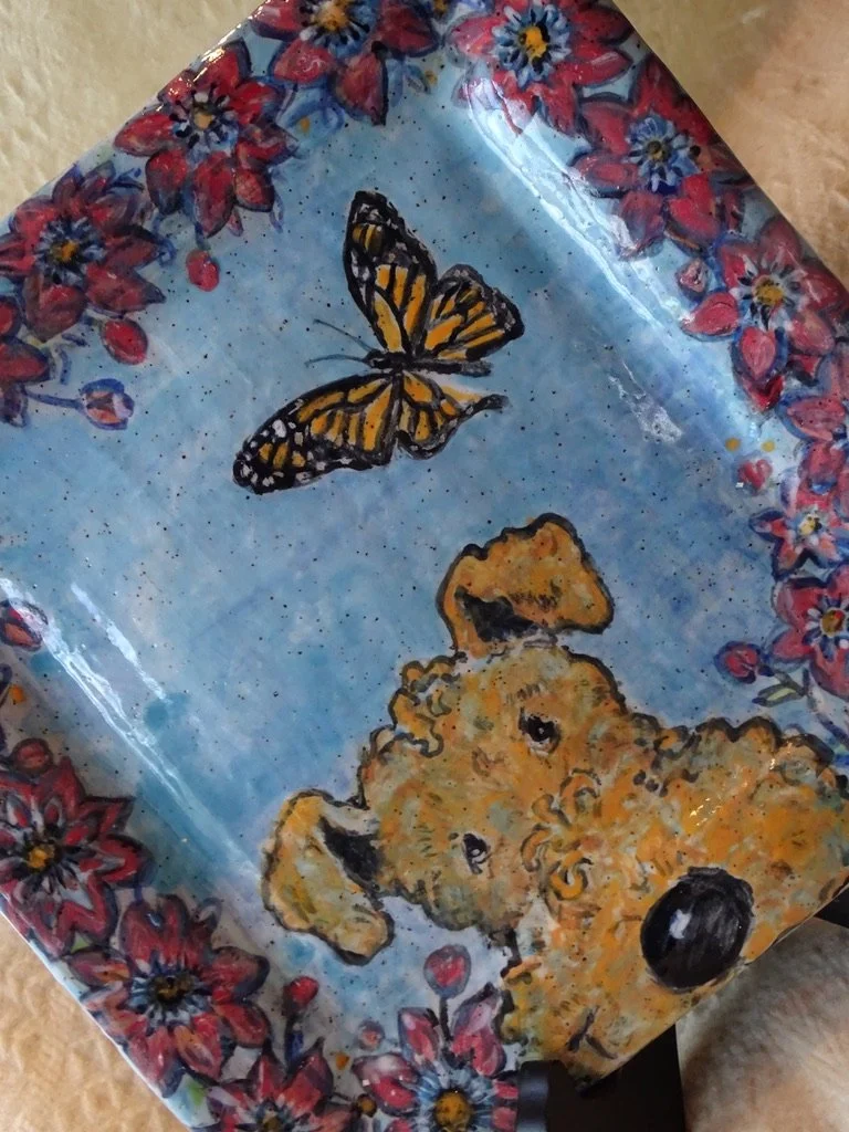 Stoneware tray with a painted image of a fluffy Airedale Terrier puppy and a Monarch butterfly, decorated with pink and purple Clematis flowers around the edges.
