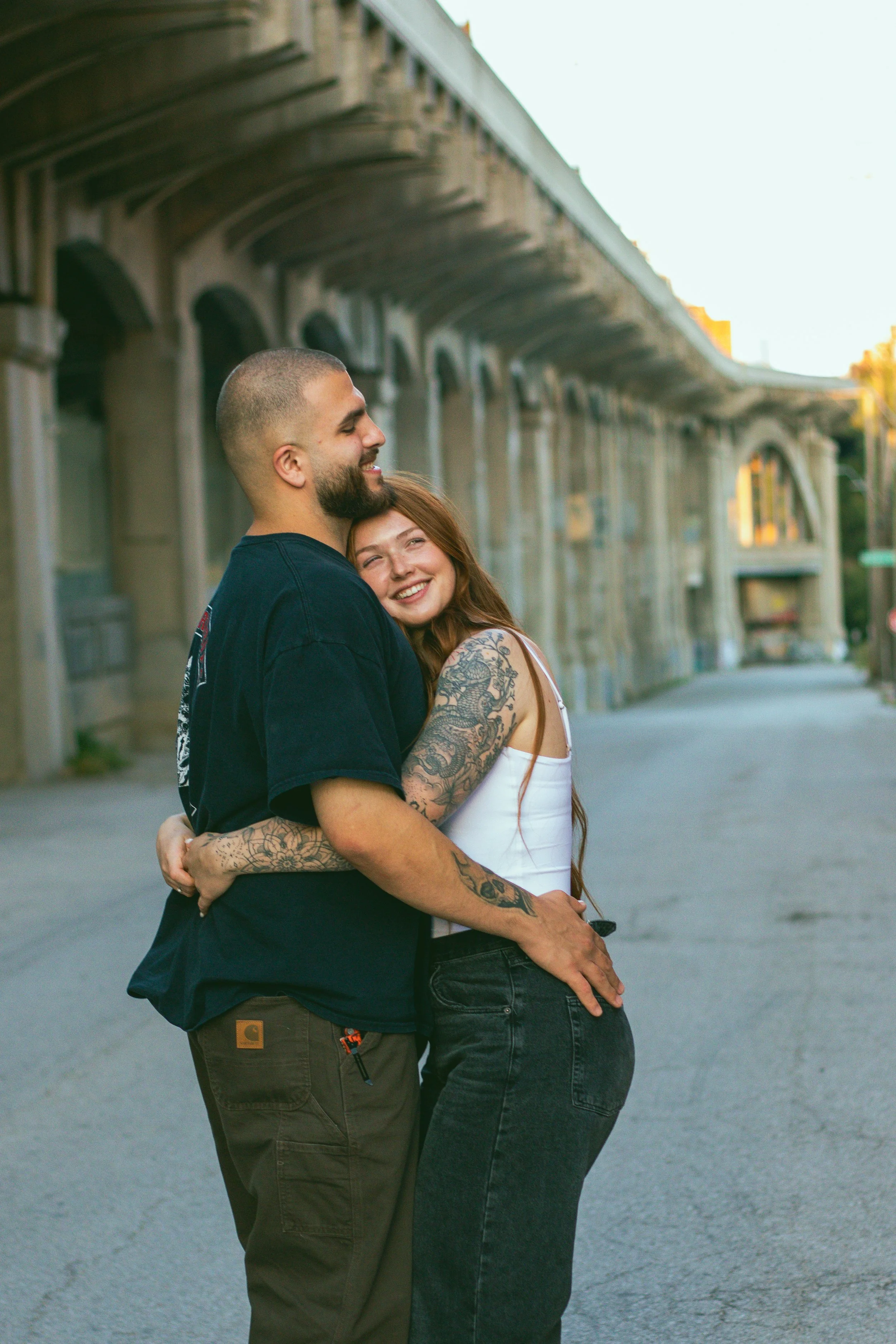 A couple hugging each other and smiling on an empty street with the Royal Gorge Bridge in the background during sunset.