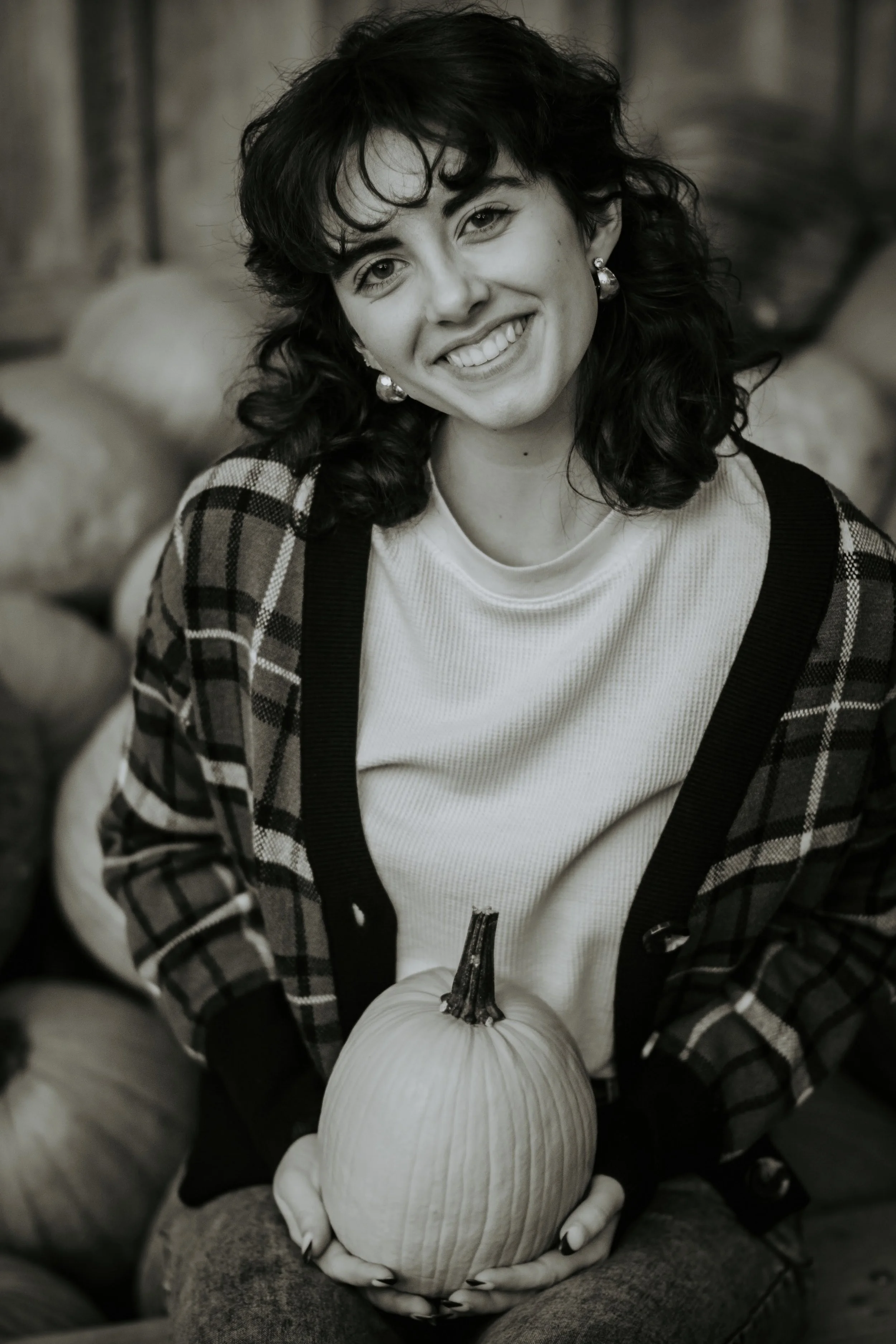 A woman with curly hair and earrings is smiling and holding a pumpkin in her hands.