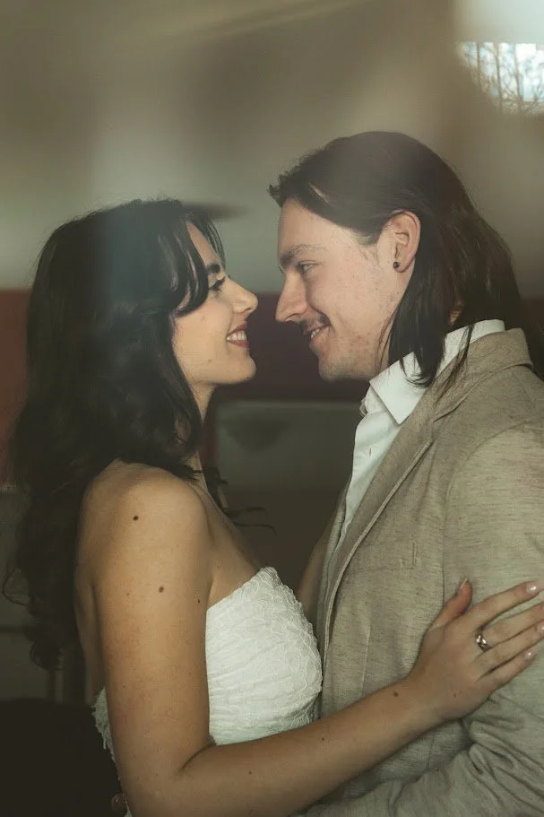 A couple smiling and gazing into each other's eyes, standing close together in an intimate moment.