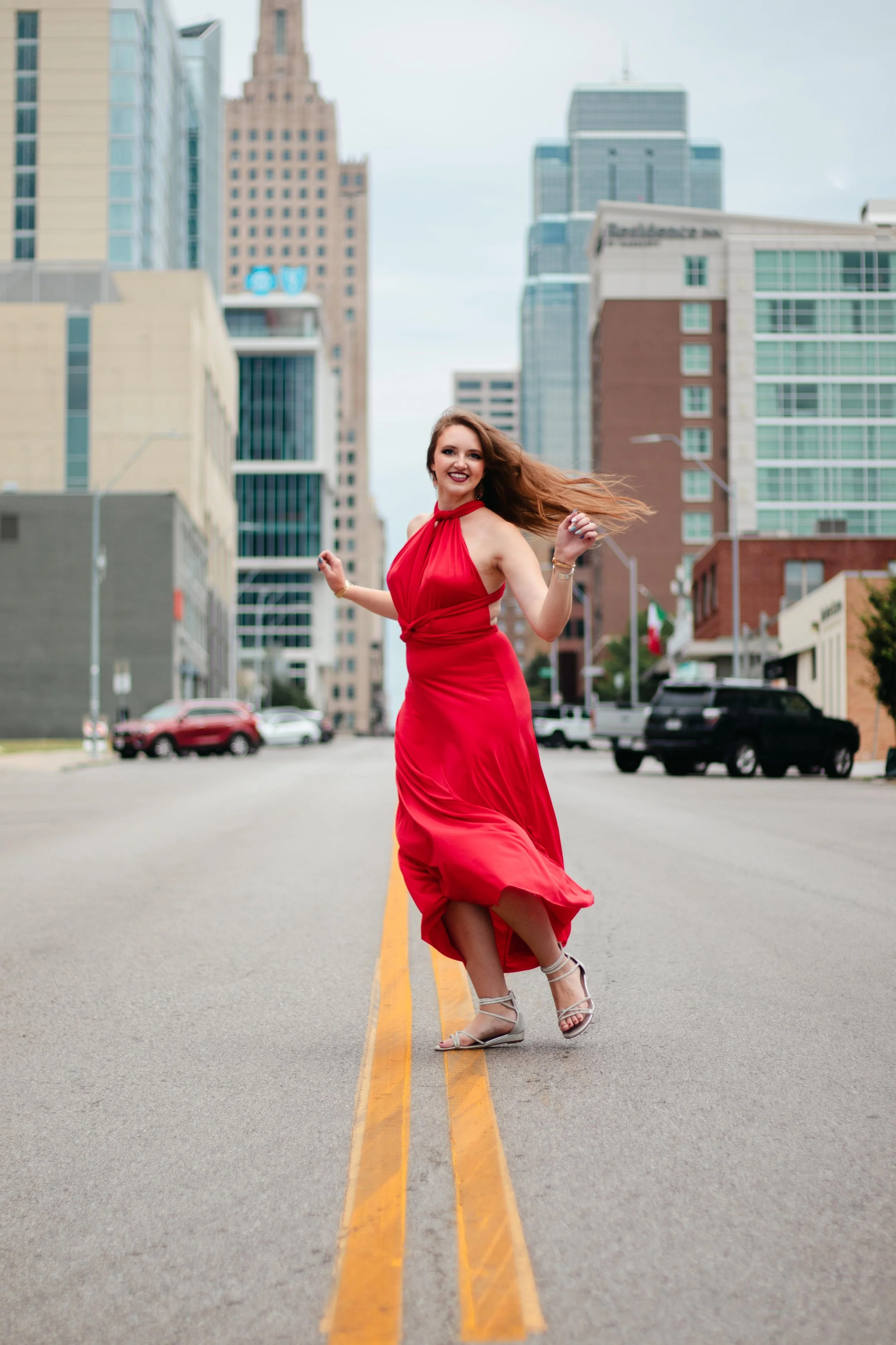 A woman in a red dress dancing in the middle of a city street with tall buildings in the background.