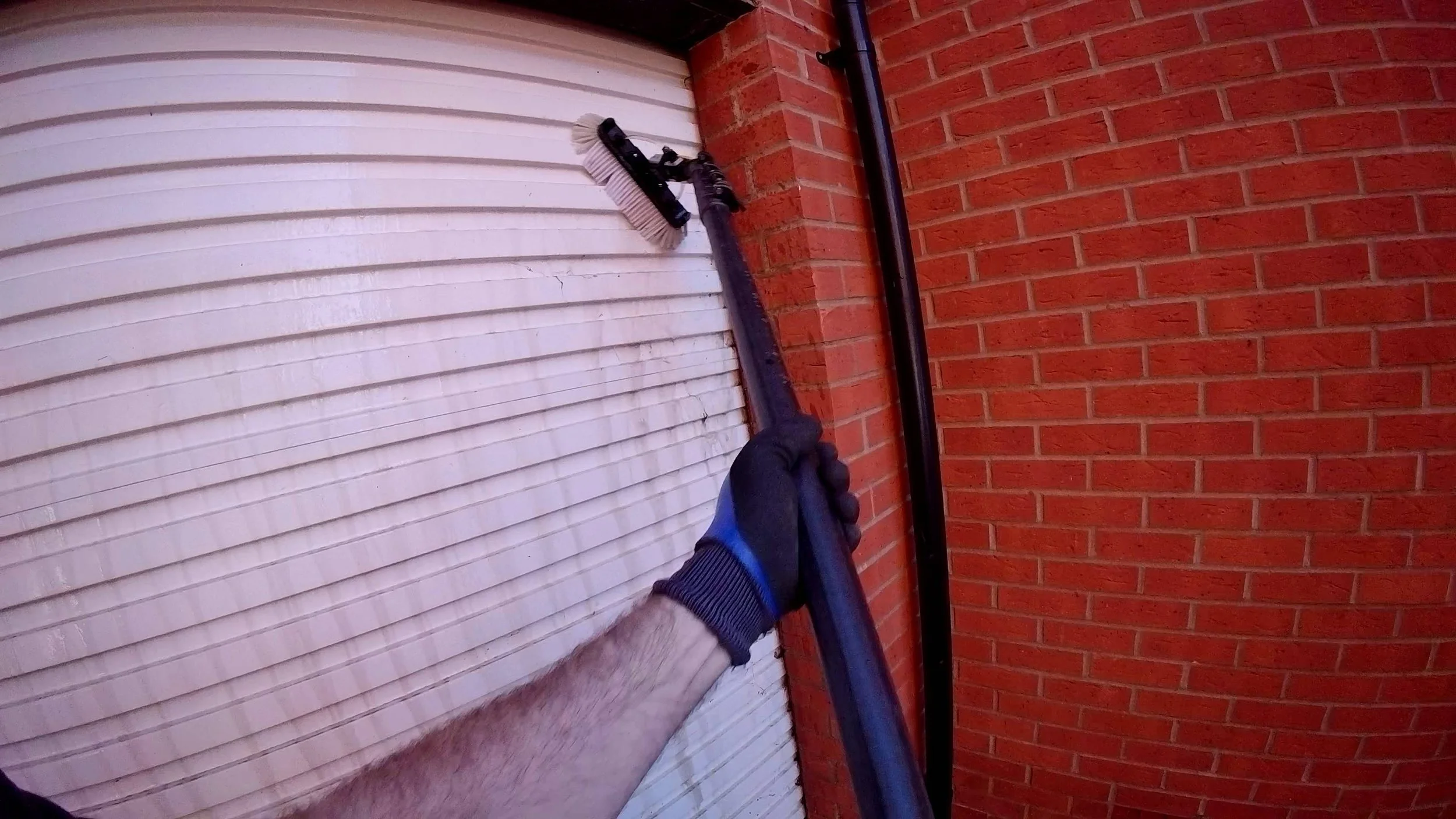 Manual garage door cleaning in Colchester using a water-fed pole and specialist brushes.