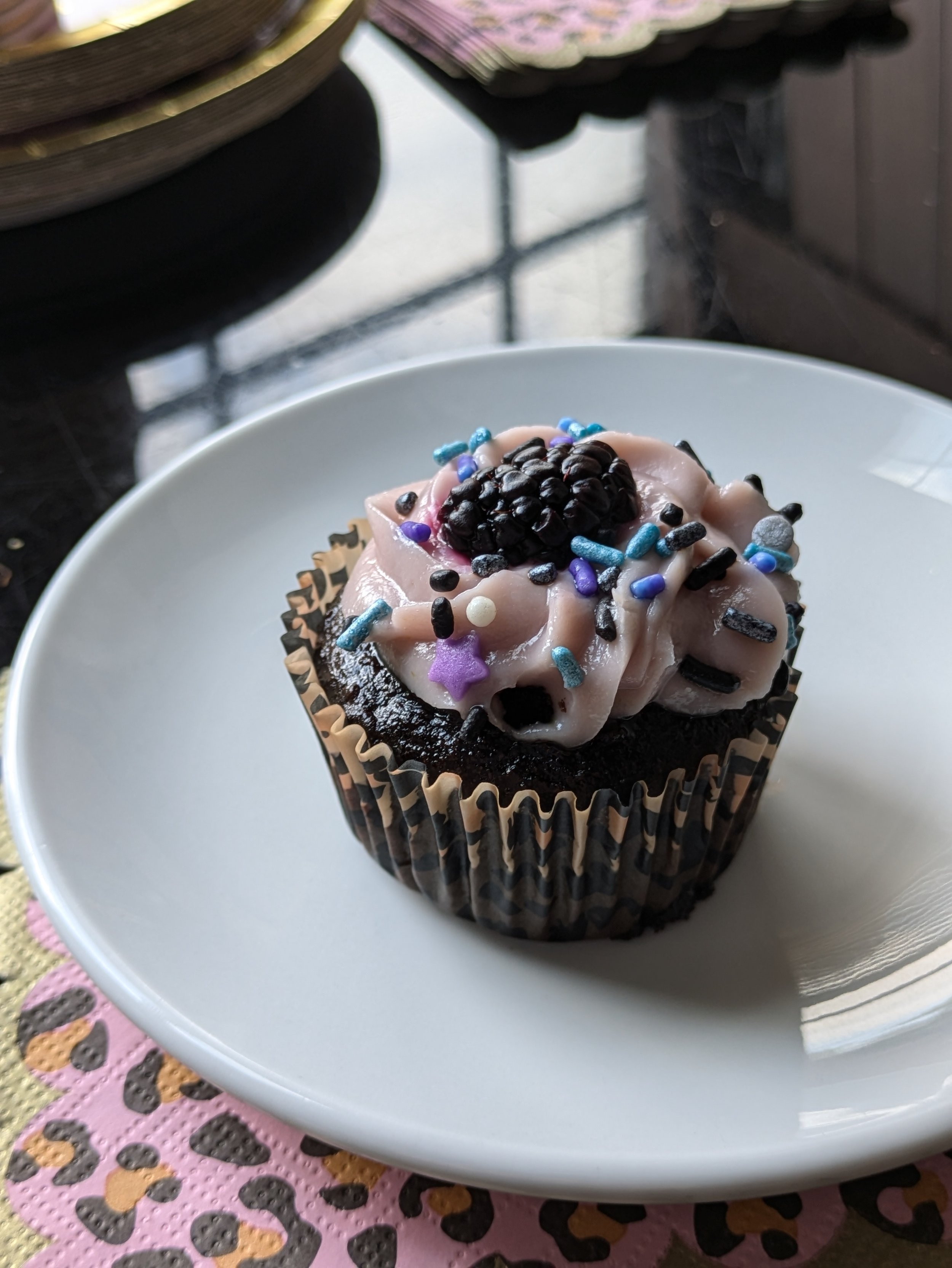 A single gluten-free chocolate cupcake with black-raspberry cream cheese frosting, star sprinkles, and a single blackberry on top