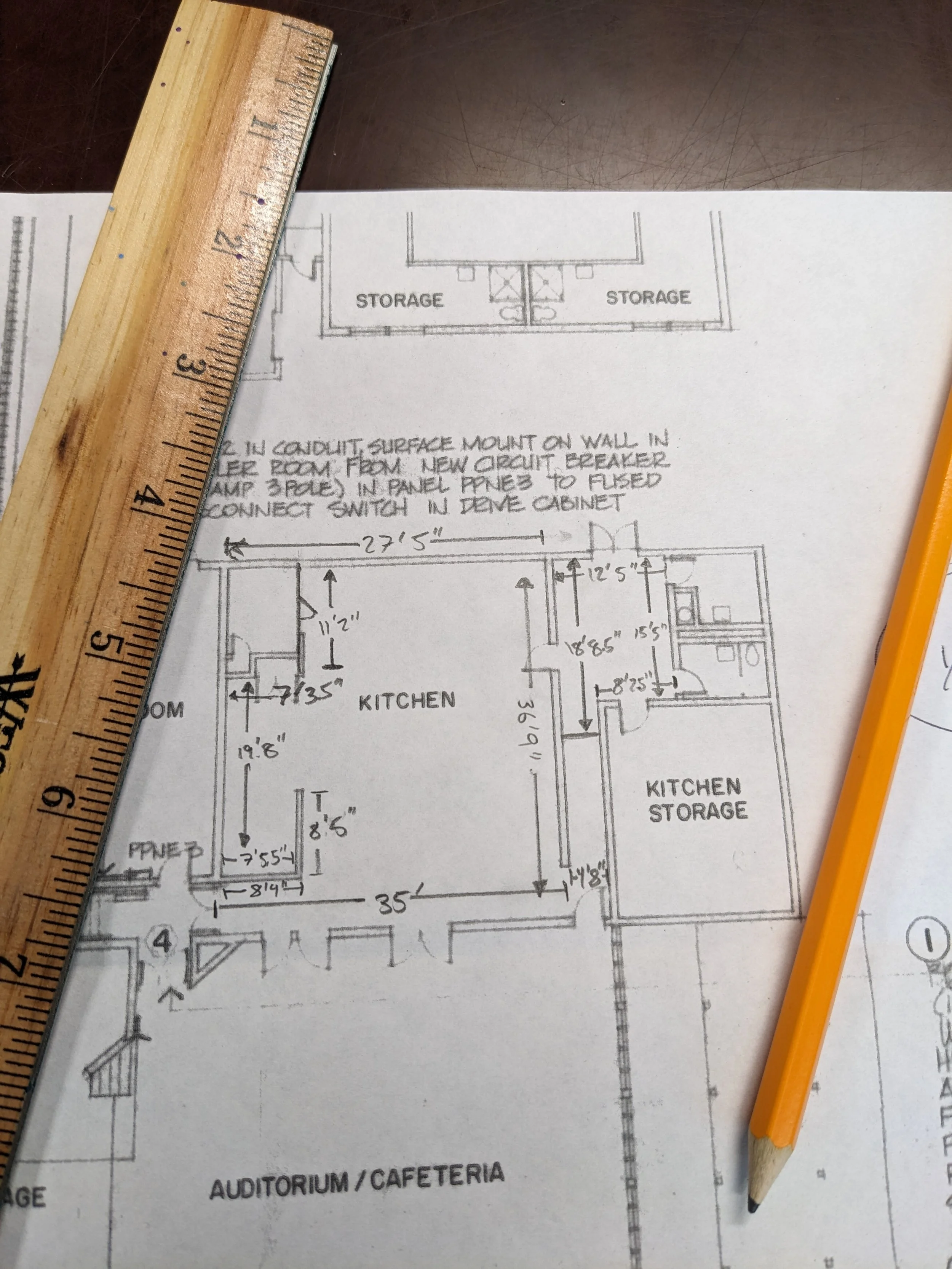 An architectural drawing of a commercial kitchen facility, with a ruler and pencil laid on top