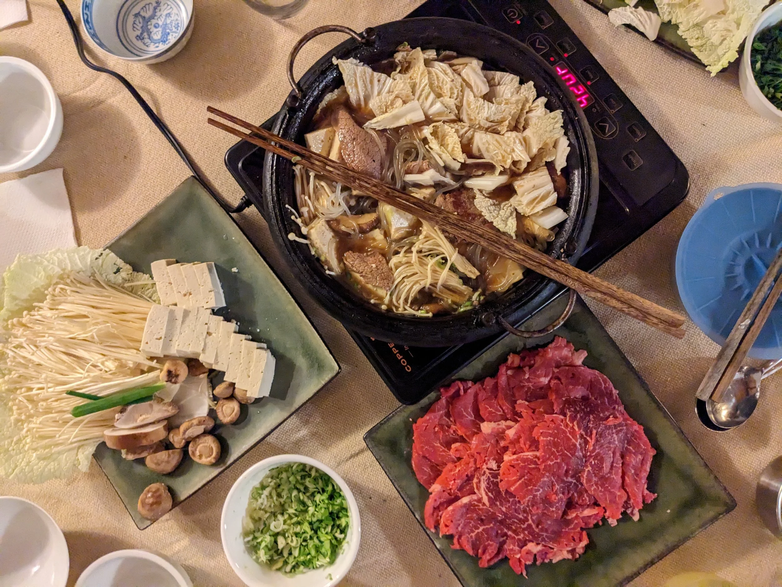 Plated prep for a hot pot dinner - sliced beef, mushrooms, tofu, green onion, cabbage, and sauce