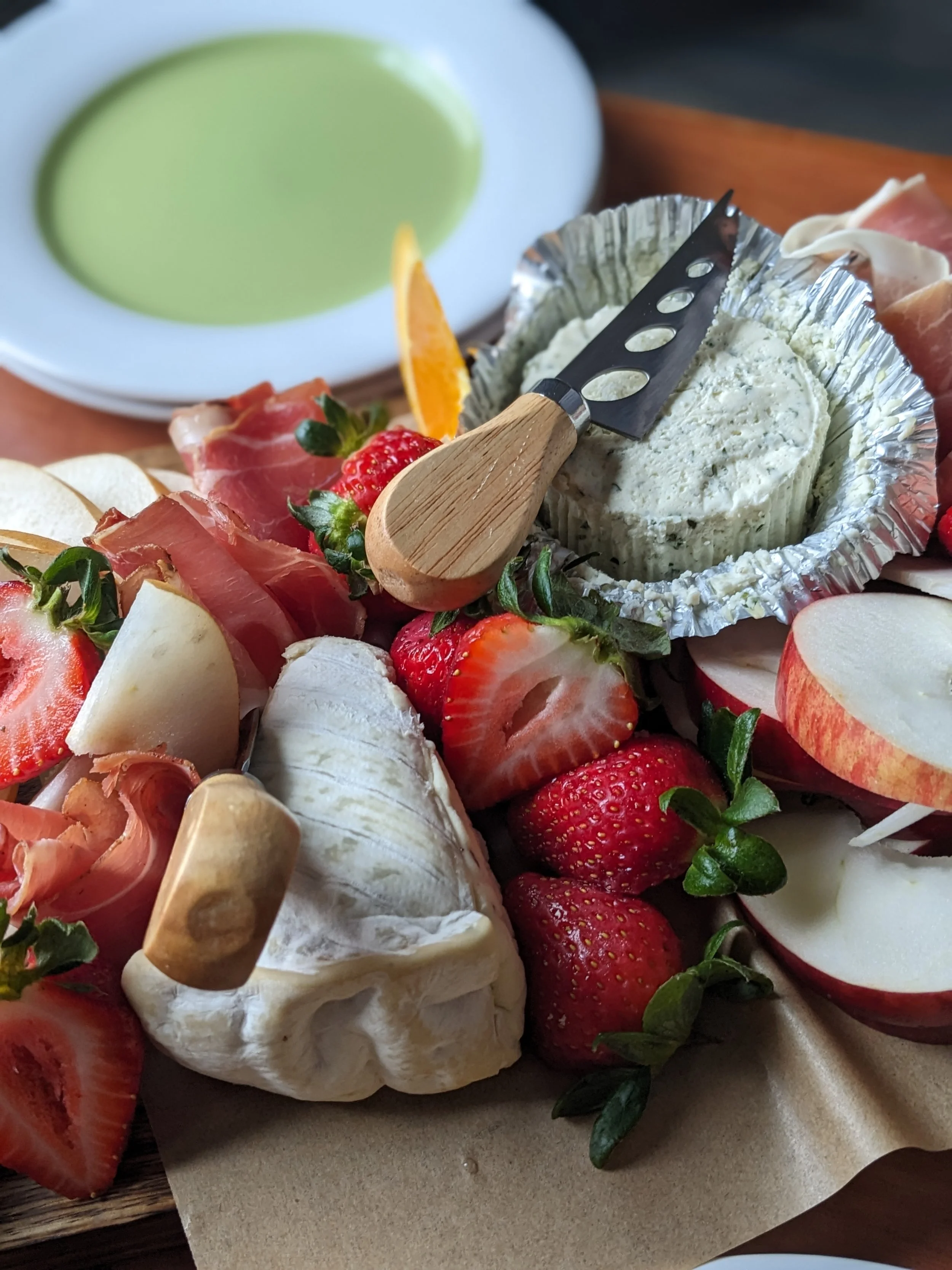 A cheese board with fresh sliced fruit and prosciutto