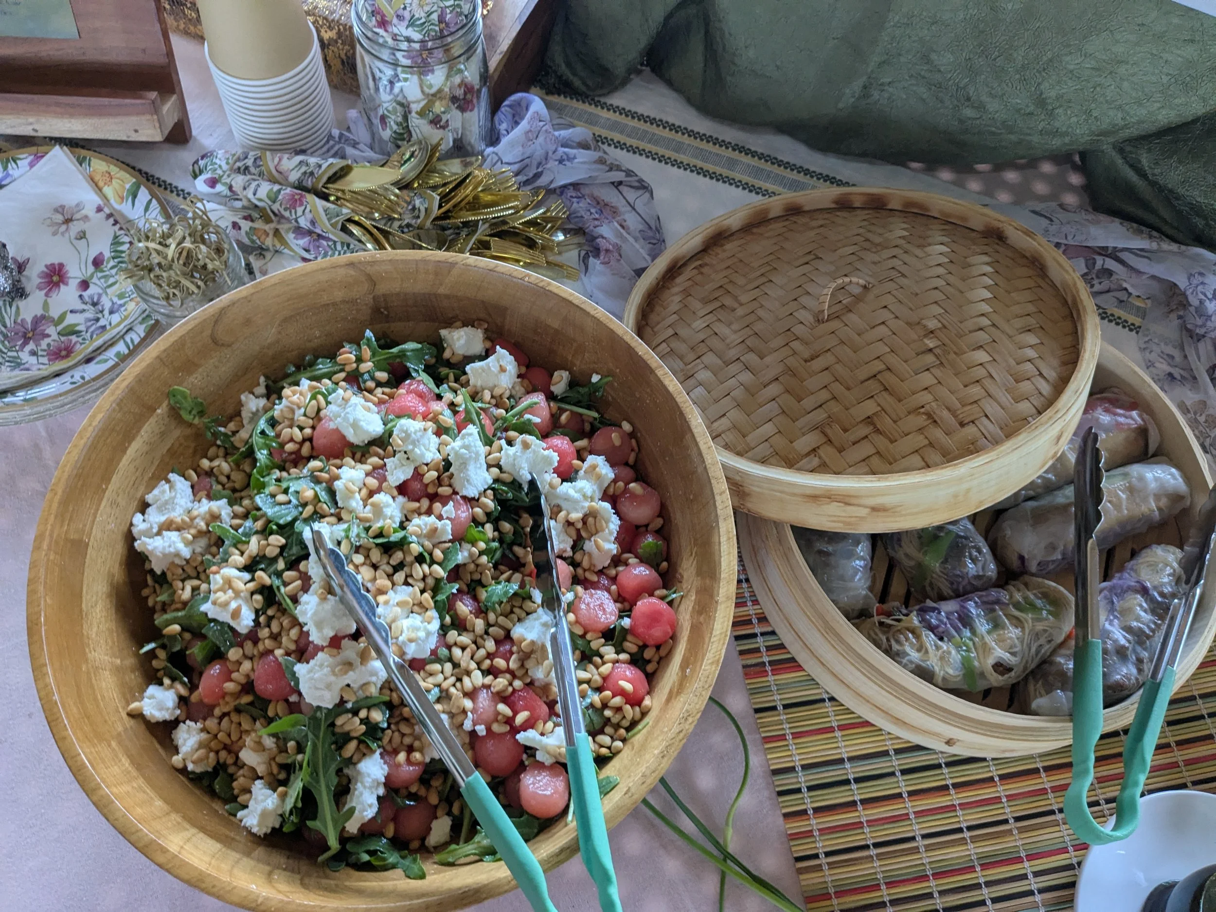 A bowl of watermelon salad and a bamboo tray of fresh spring rolls