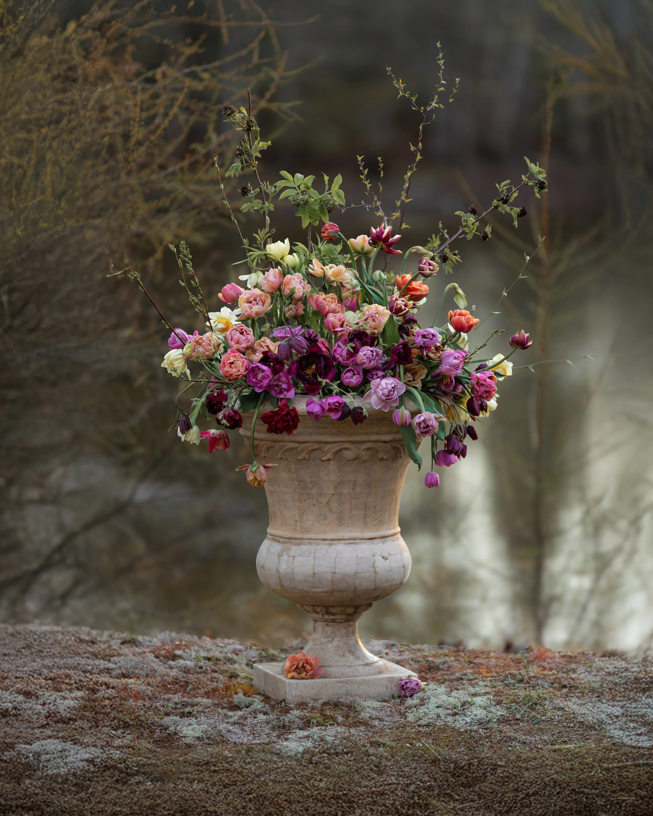 Un arrangement floral coloré dans une urne en pierre, placé sur une surface rocheuse en plein air.