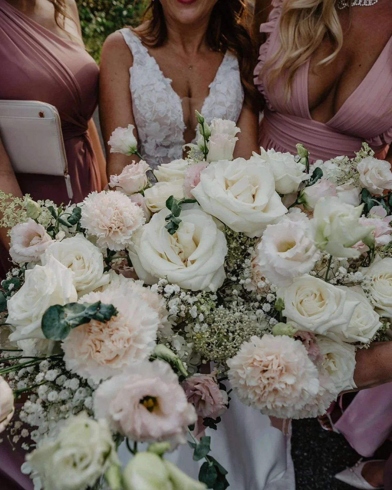 Un groupe de femmes portant des robes roses et une femme en robe blanche, tenant un grand bouquet de fleurs blanches et roses lors d'une célébration ou d'un mariage.