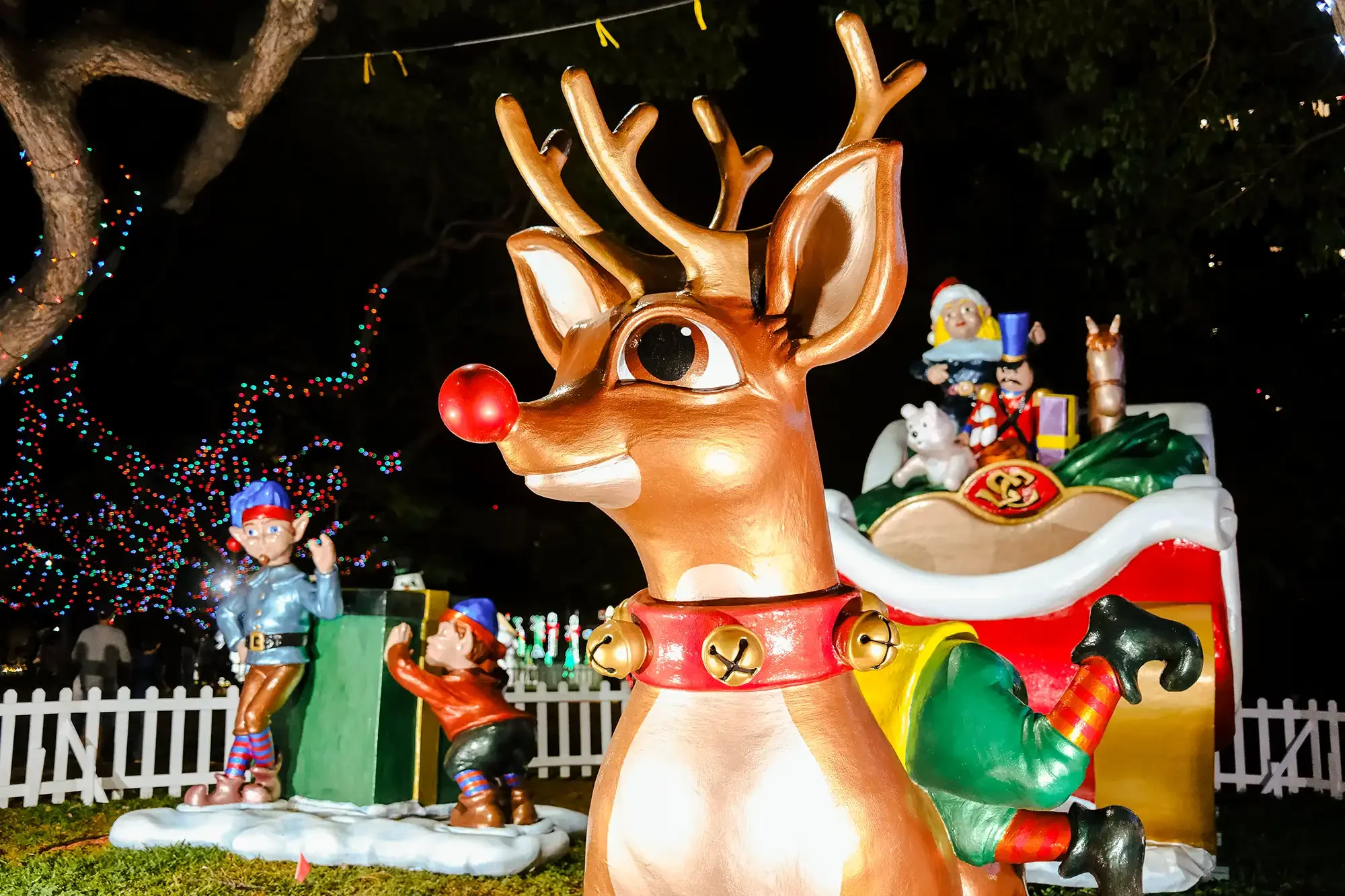 At the Honolulu City Lights, Christmas display with a large reindeer figure with a red nose and elf and toy soldier figures in a Santa's sleigh background, decorated with colorful holiday lights.