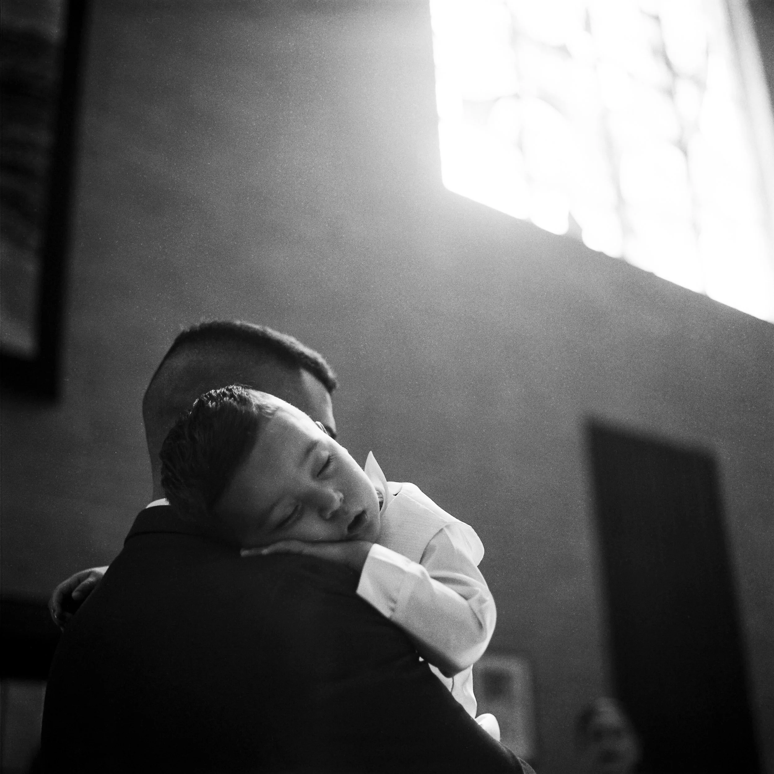A man holding a sleeping child in a loving embrace in a softly lit room.