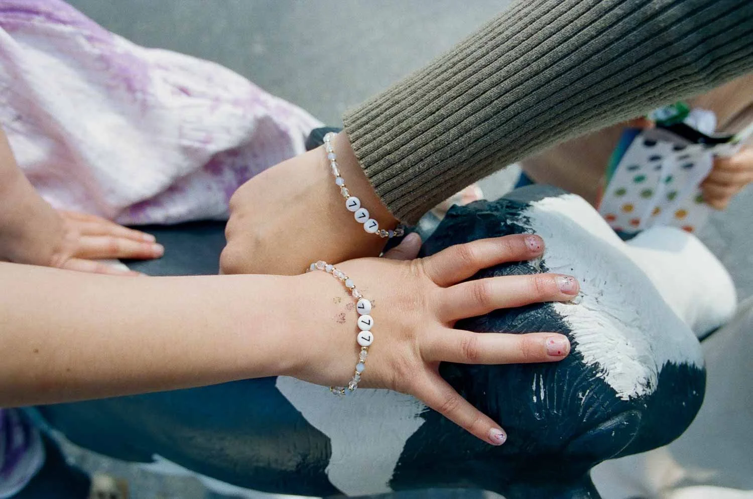 Two people with matching letter bracelets on their wrists, holding onto a painted cow statue.