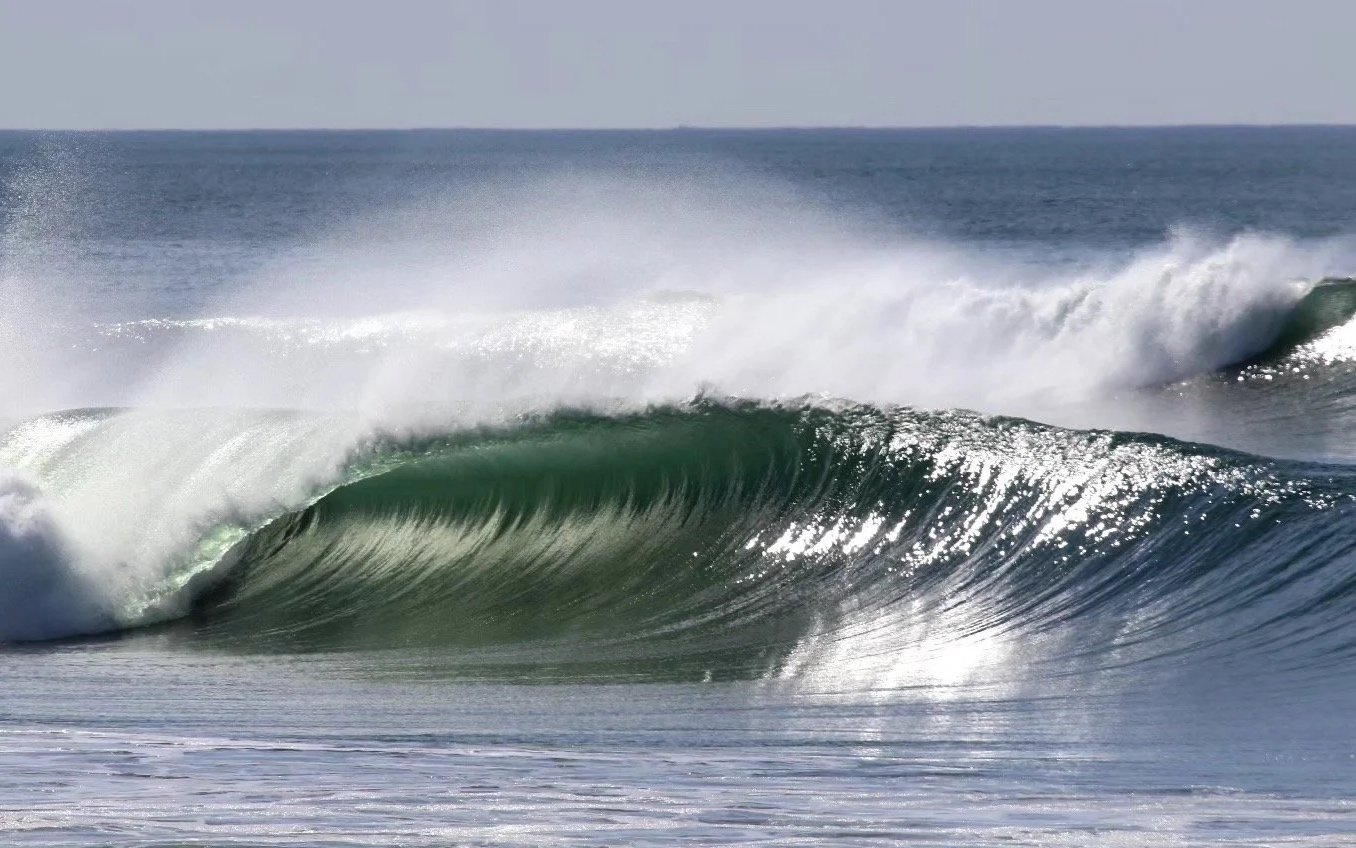 Perfect hollow left pealing ocean wave crashing with white spray in the background.