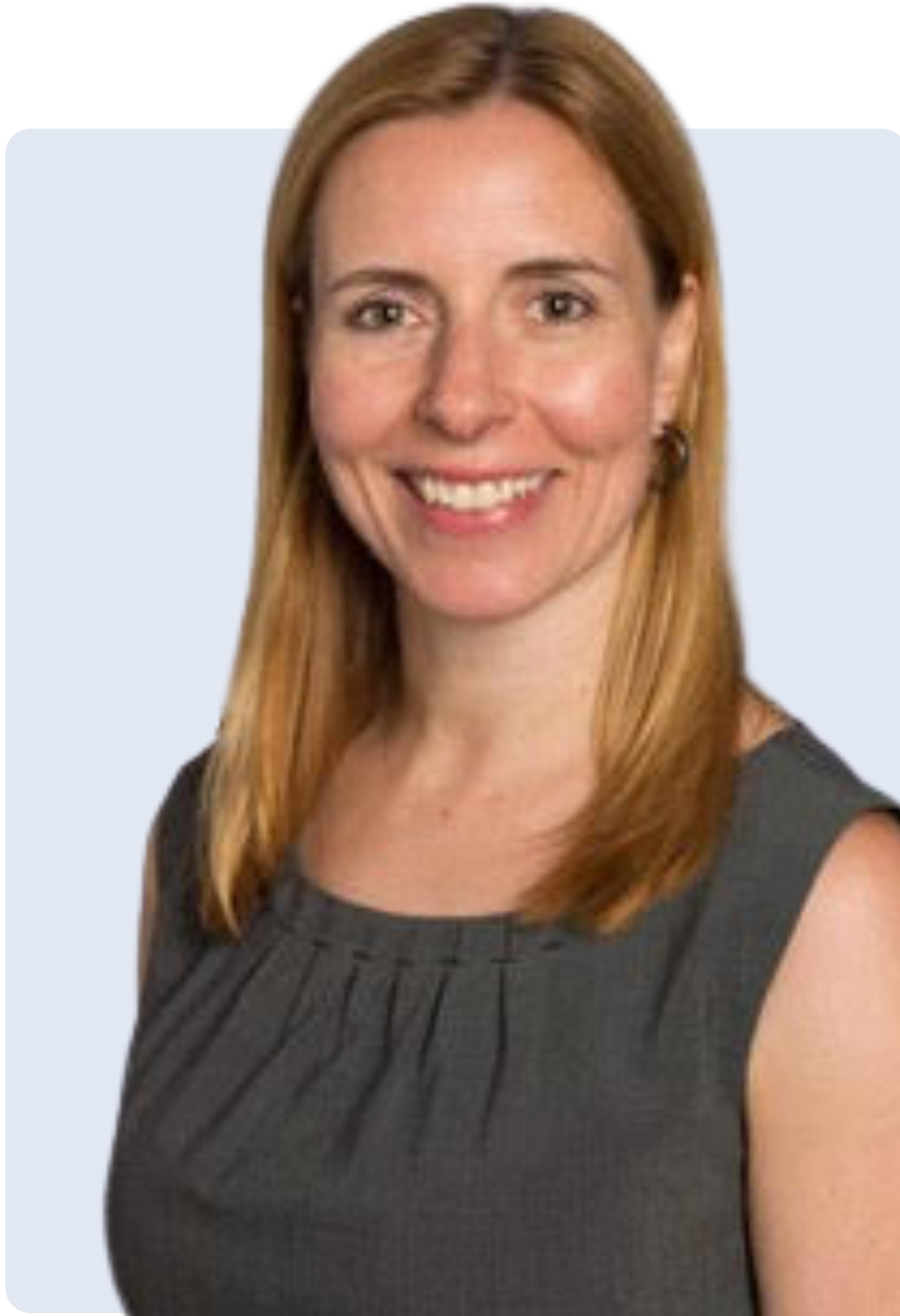 A woman with shoulder-length red hair, smiling, wearing a sleeveless dark gray dress and earrings, against a blue background.