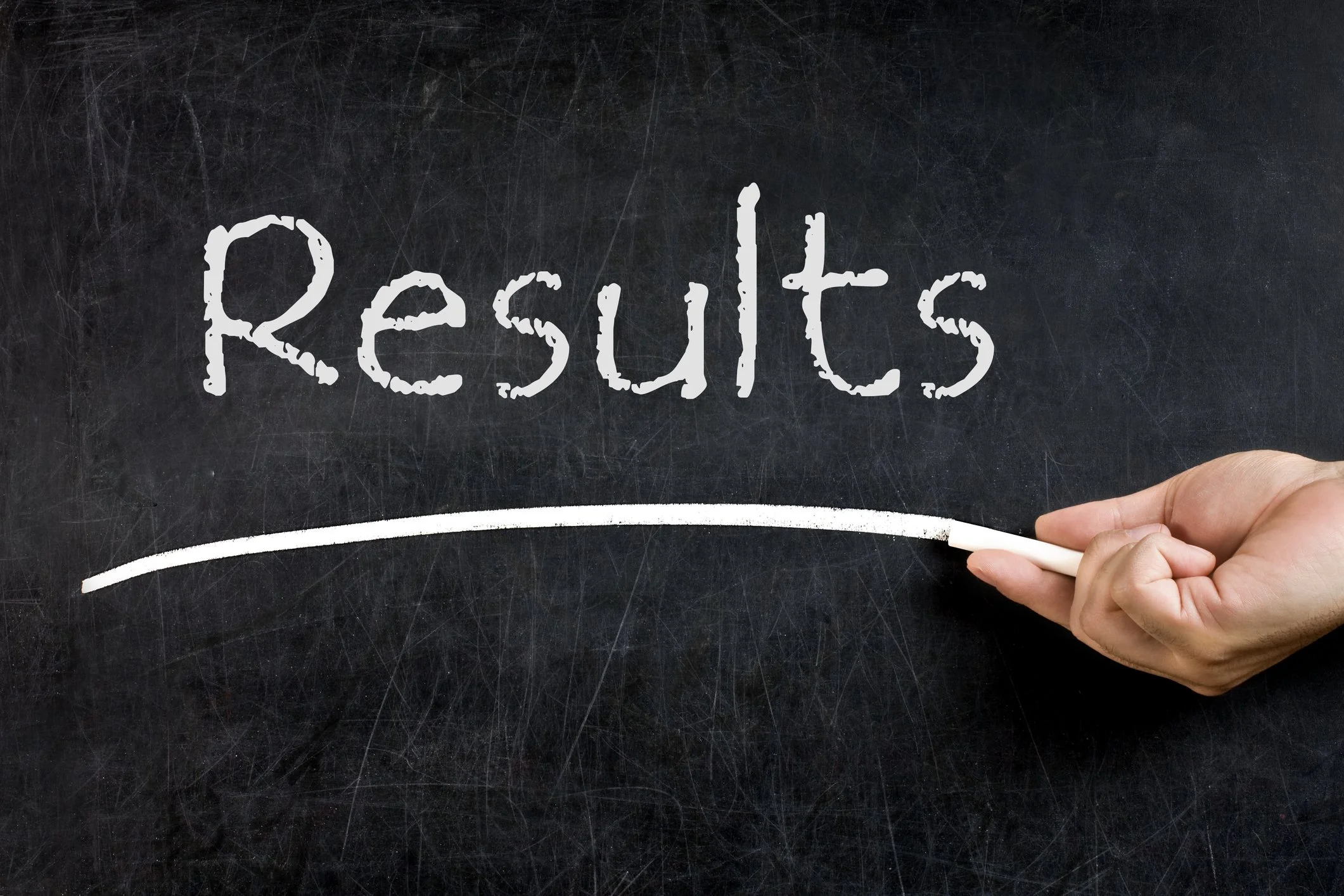 Hand holding chalk under the word 'Results' written on a black chalkboard.