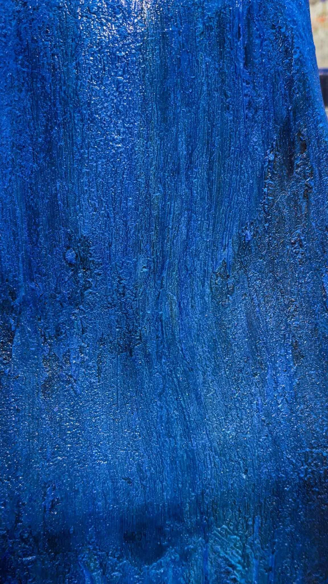 Close-up of a textured blue painted surface with visible brush strokes and water droplets.