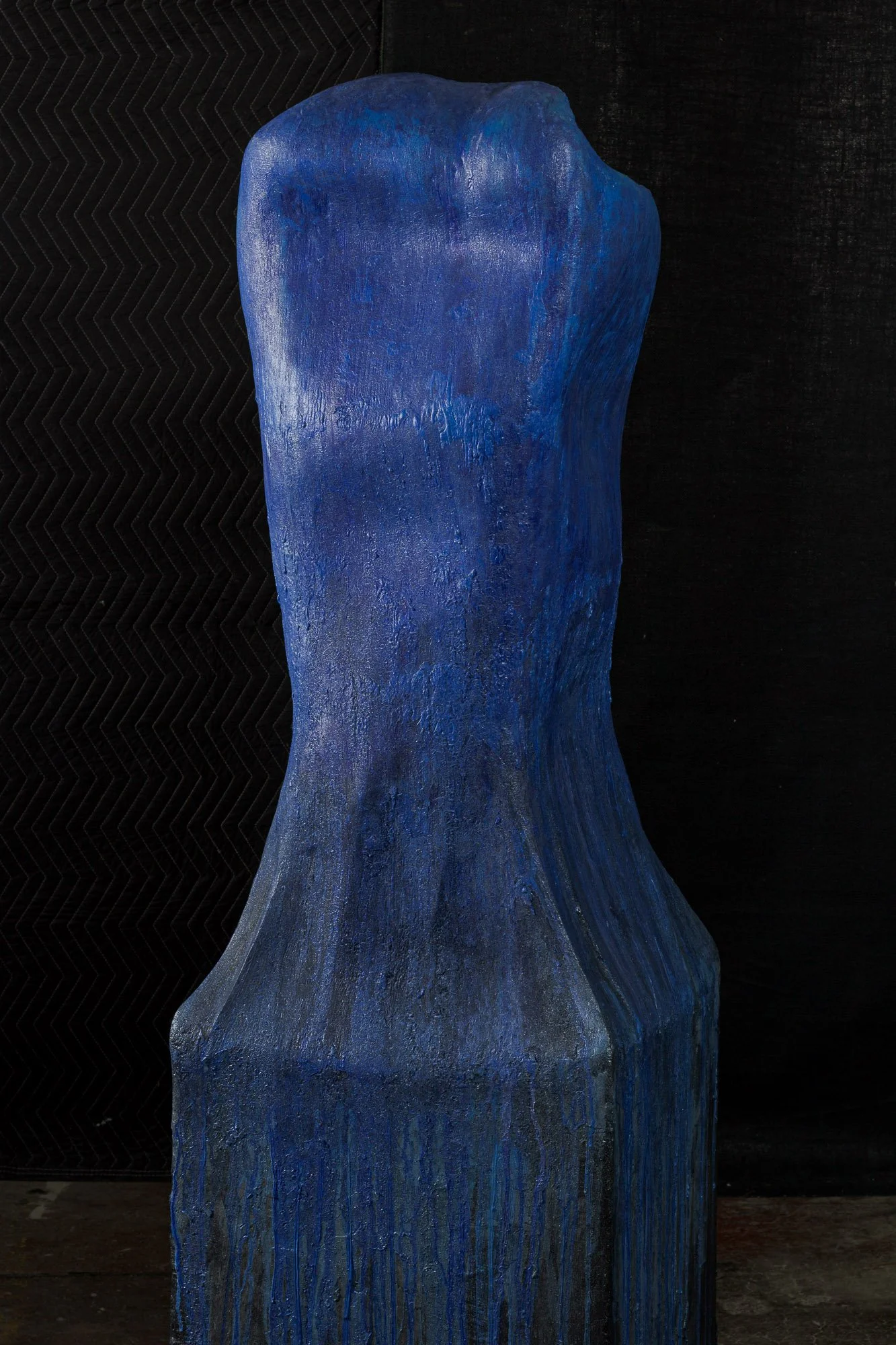 A tall, blue sculptural piece with flowing, irregular shape against a dark background.