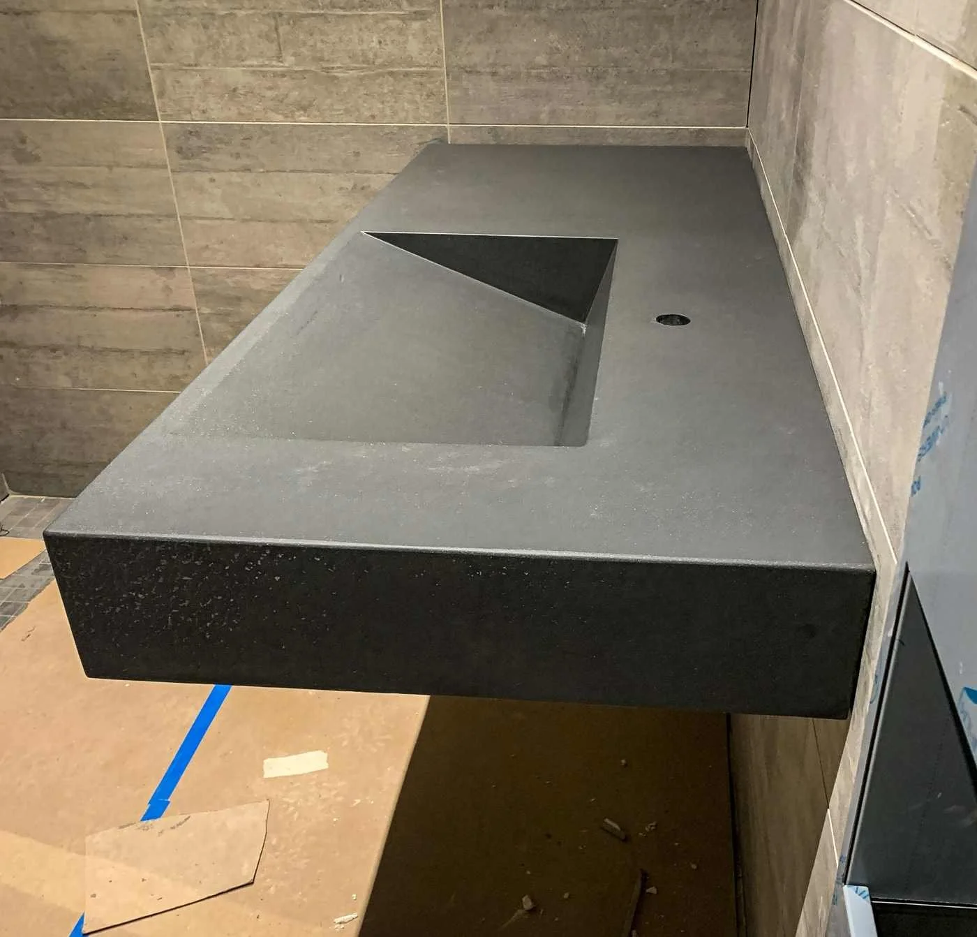 Wall-mounted custom cast concrete sink with integrated basin in a tiled commercial restroom.